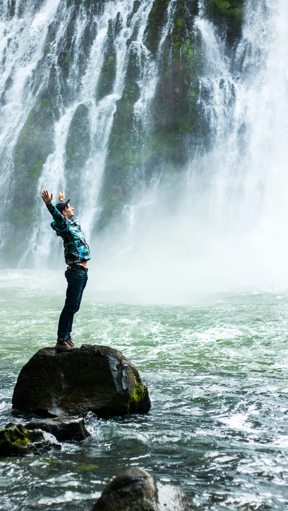 Man on rock in front of waterfall with arms outstretched inpose of freedom and happiness
